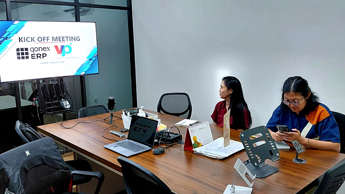 Suasana kick off meeting di ruang rapat; layar TV menampilkan slide Kick Off Meeting dengan logo Qonex ERP dan vCloudProperty+ bertanggal Jumat, 14 Agustus 2026, dua peserta duduk di meja rapat kayu dengan laptop dan dokumen.