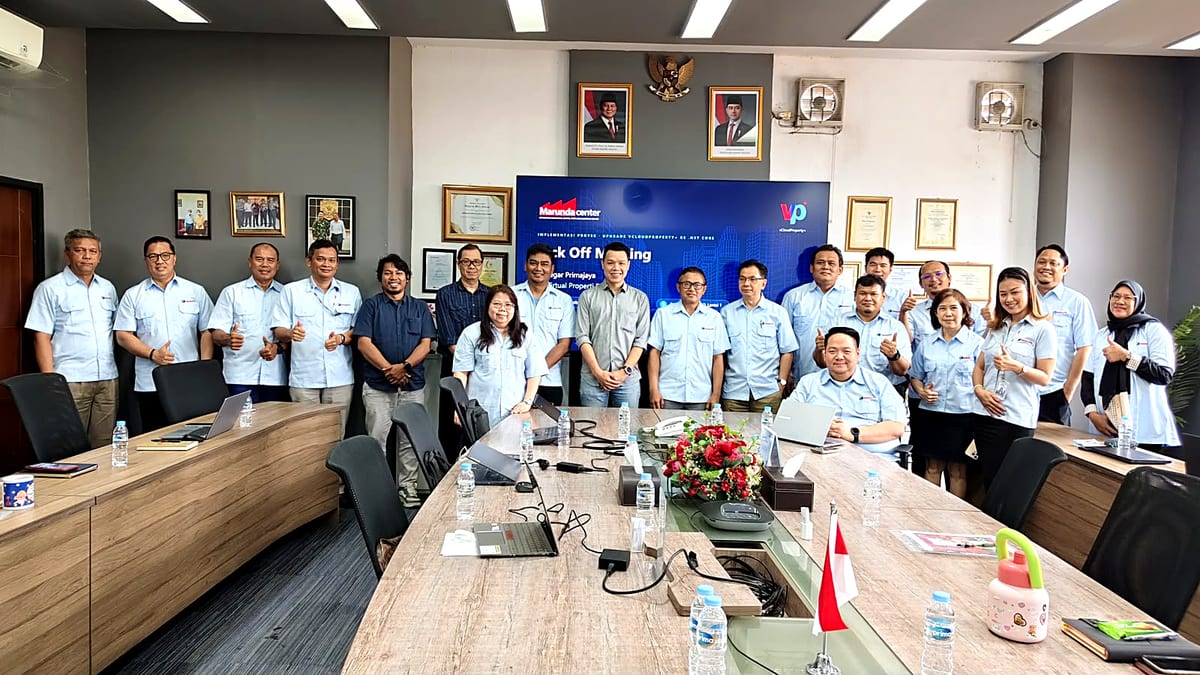 Sekitar dua puluh orang, sebagian besar berseragam biru muda, berdiri dan mengacungkan jempol di ruang rapat di depan layar bertuliskan Kick Off Meeting dengan logo Marunda Center dan vCloudProperty+.