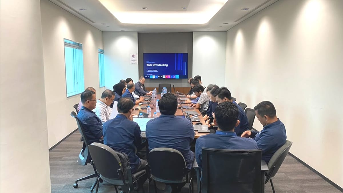 Ruang rapat berisi sekitar 15 peserta berseragam biru duduk mengelilingi meja panjang, menghadap layar bertuliskan Kick Off Meeting.